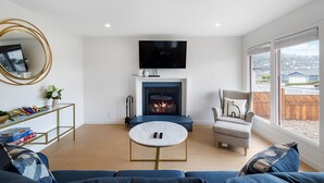 Ein modernes Wohnzimmer mit Kamin, Fernseher und einem großen Fenster mit Blick nach draußen.