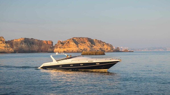 A boat on calm water with rocky cliffs in the background.