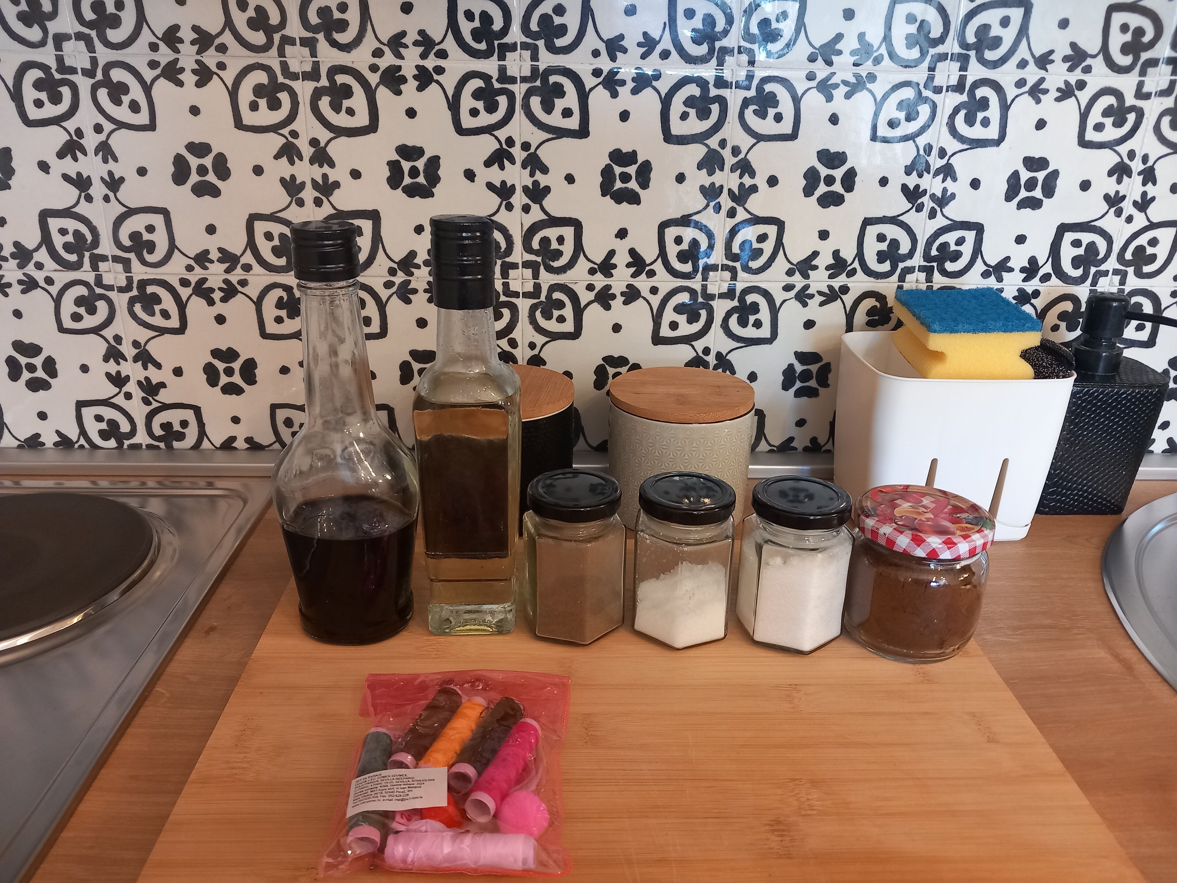 A kitchen counter with various items including bottles, jars, and a package of thread.