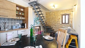 Une cuisine avec un plan de travail en bois, une table à manger dressée avec des assiettes et des couverts, un escalier et un mur en pierre.