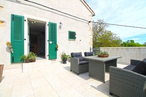 An outdoor patio with wicker furniture, a tiled floor, and a building with green shutters. - Studio apartment 2323/109271 (Istria - Svetvinčenat), 28500m from the beach (Svetvinčenat)