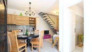 Un espace repas avec une table ronde, des chaises en bois et un lustre. Un escalier mène à un niveau supérieur.