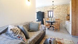 Un salon chaleureux avec un canapé, une table à manger et un coin cuisine aux murs en pierre.