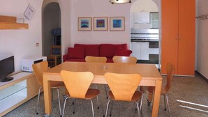 Ein Essbereich mit Tisch und Stühlen, eine rote Couch, eine Küche im Hintergrund und eine Deckenleuchte.