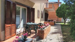 Eine Terrasse mit Tisch und Stühlen, ein Ziegelkübel mit Blumen und ein überdachter Sitzbereich mit Tisch und Stühlen.