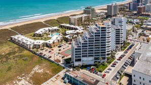A coastal hotel with multiple buildings, a parking lot, and a beach view.