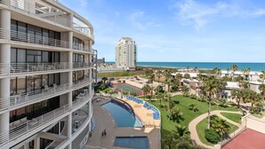A multi-story hotel with a rooftop pool, outdoor seating, and a view of the beach and ocean.