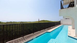Piscina com vista para o oceano, cercada por uma grade preta e um edifício branco.