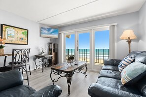 Un soggiorno con vista sulla spiaggia, una zona pranzo con tavolo e sedie e un divano con cuscini decorativi.