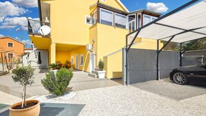 A yellow building with a covered carport and potted plants in the foreground.