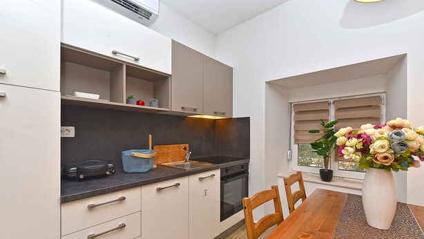 A modern kitchen with white cabinets, a wooden dining table, and a vase of flowers.