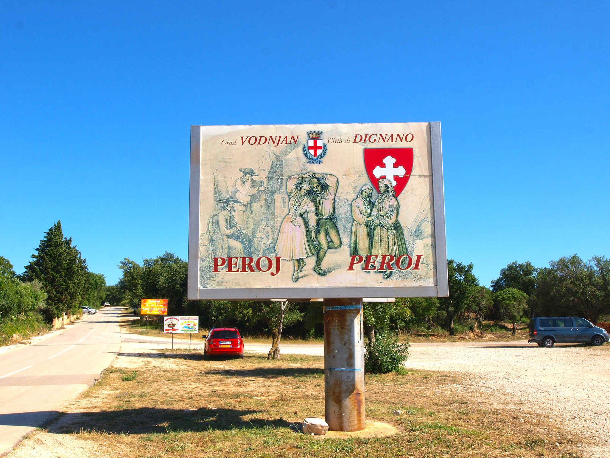 A historical sign with figures and text, located beside a road with vehicles.