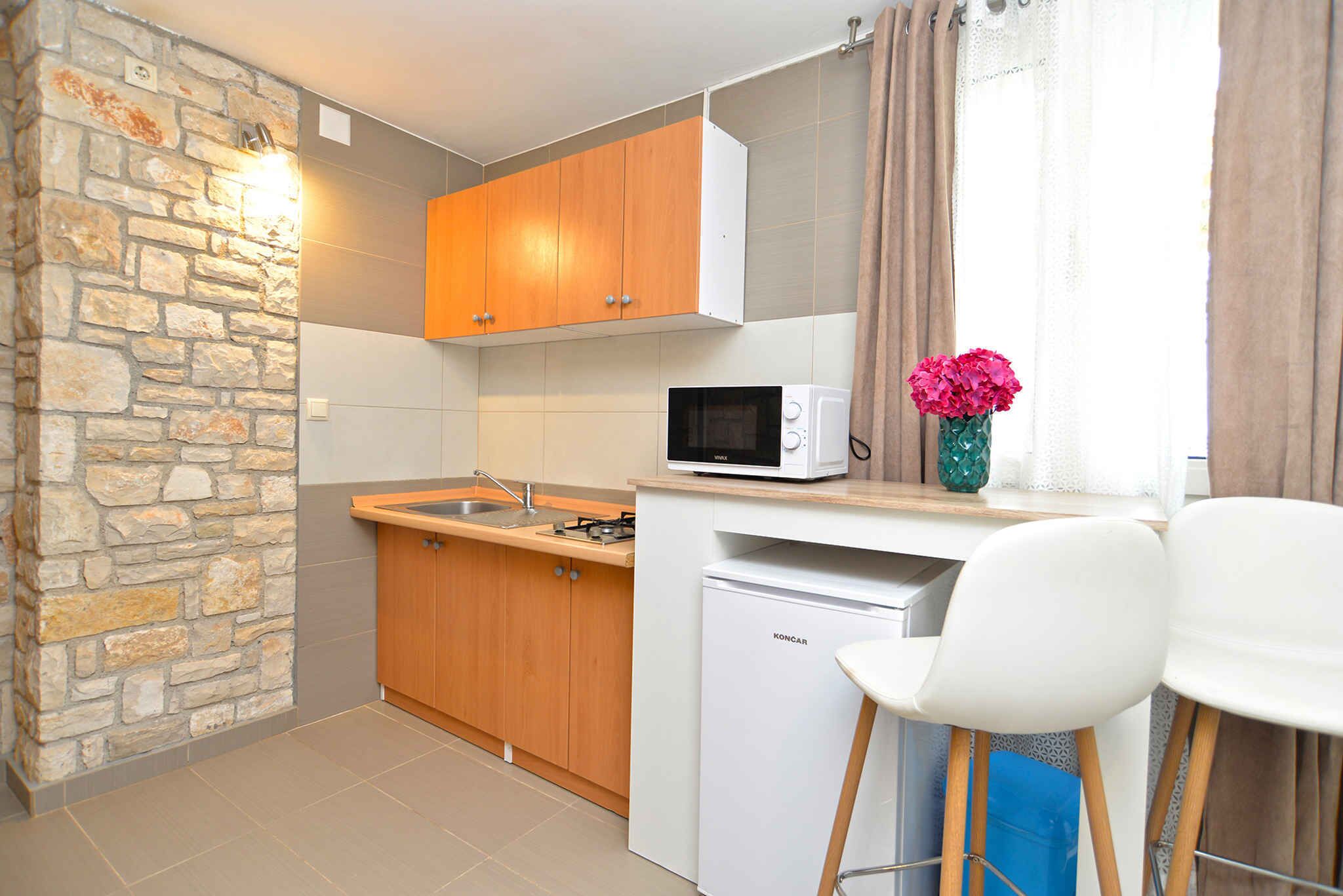 A compact kitchen with a stone wall, wooden cabinets, a microwave, and a small refrigerator.