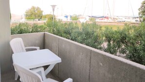 Een balkon met een witte tafel en twee witte stoelen, met uitzicht op een jachthaven vol boten.