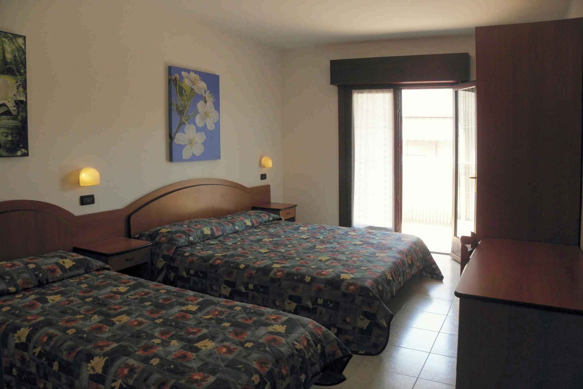 A hotel room with two beds, a desk, a chair, a window with a view, and wall-mounted lamps.