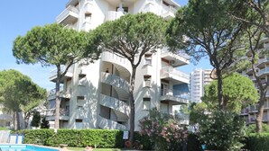 A multi-story residential building with balconies, a swimming pool, and surrounding greenery. - Holiday apartment with air conditioning and balcony (Lignano Sabbiadoro)