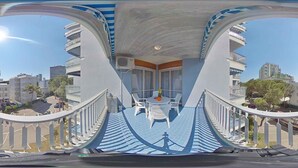 A balcony with a table and chairs, overlooking a cityscape with multiple buildings. - Holiday apartment with air conditioning and balcony (Lignano Sabbiadoro)