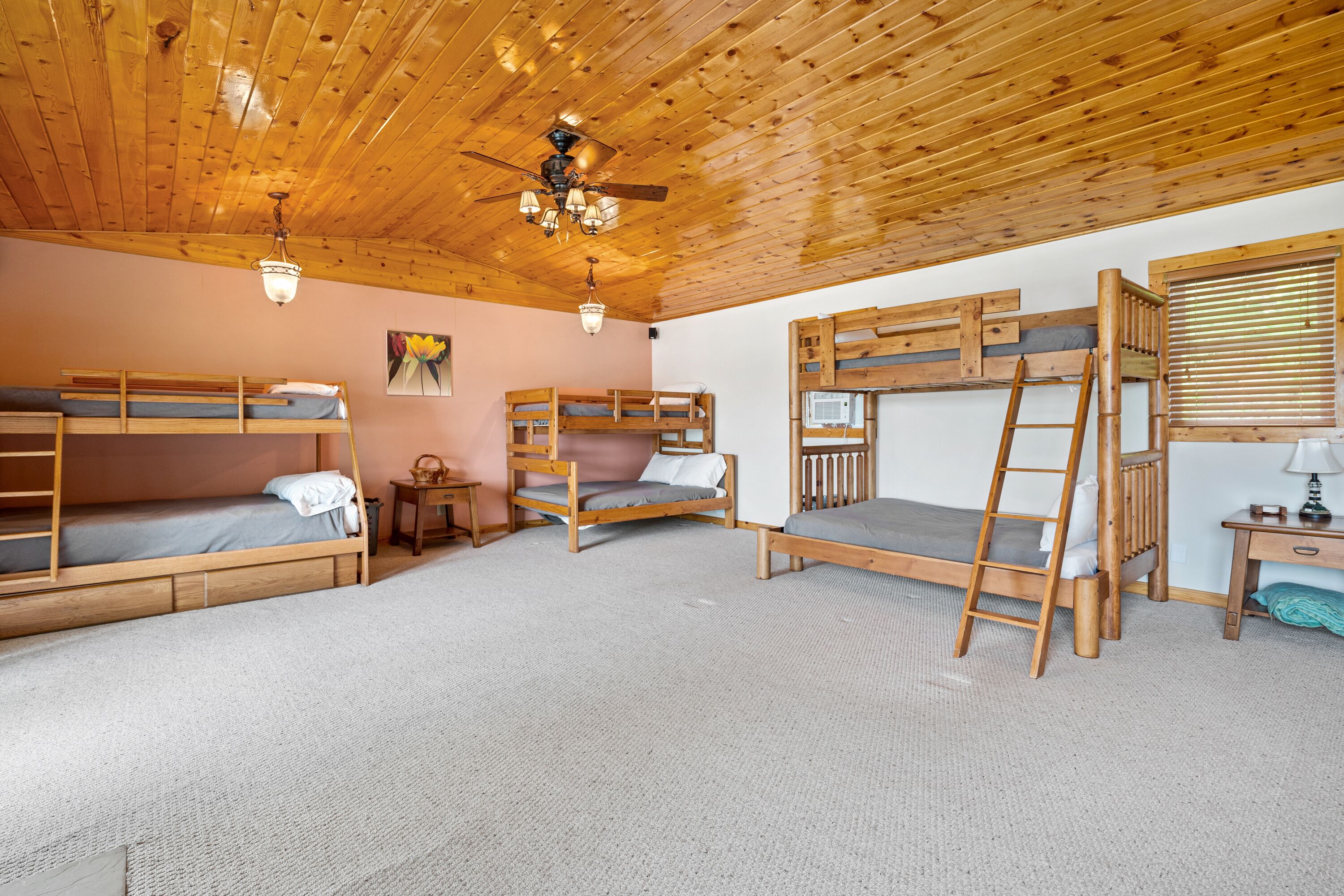 A room with bunk beds, a ceiling fan, and a small table with a lamp.