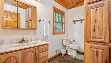 A bathroom with wooden cabinets, a marble sink, a toilet, and a window with blinds.