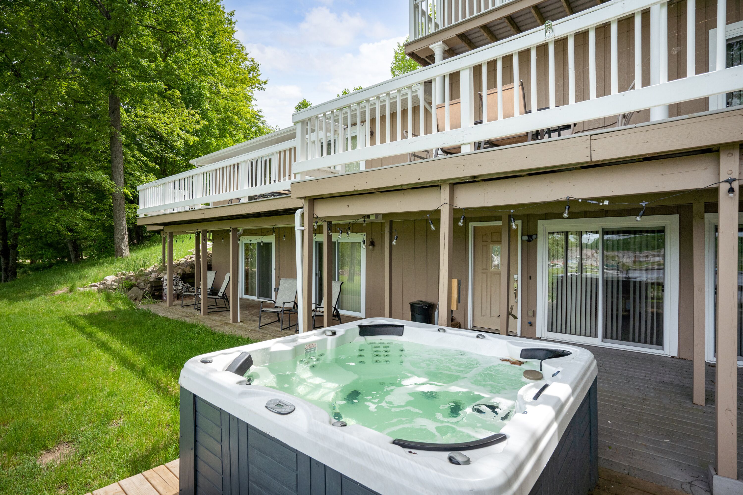 A hot tub on a wooden deck with a covered patio area and a view of a house with a balcony.