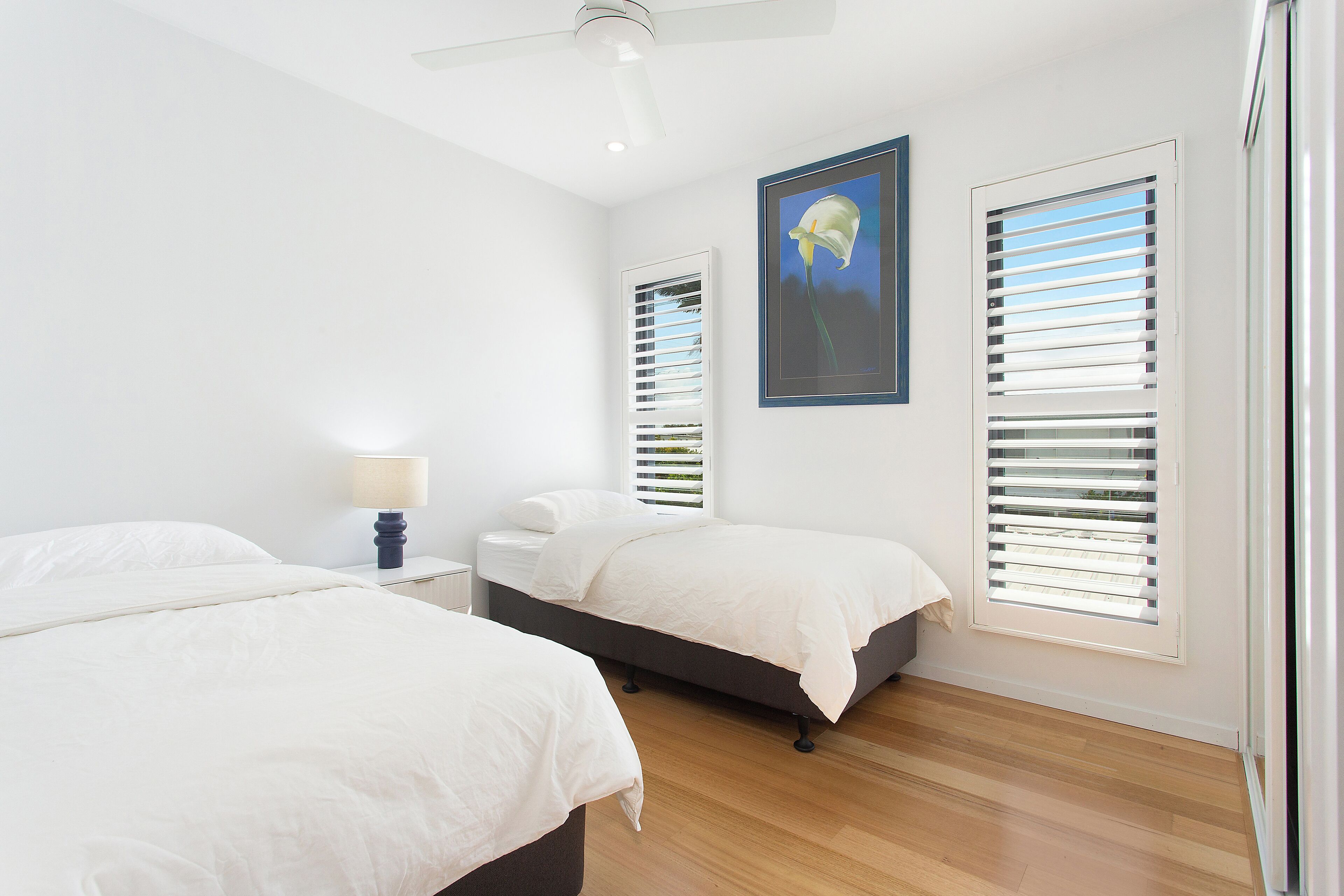 A bedroom with two beds, a ceiling fan, a nightstand with a lamp, and a framed picture on the wall.