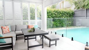 Zona relax esterna moderna con vista sulla piscina, caratterizzata da un divano, tavolini e una ringhiera in vetro.
