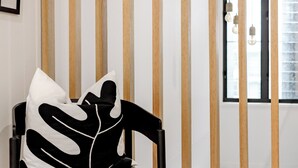 Una camera moderna con una sedia nera, un cuscino bianco e un pannello divisorio in legno a listelli.