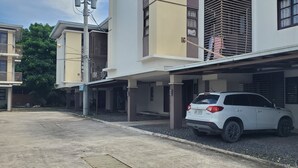 Un VUS blanc est garé dans un parking couvert d’un immeuble moderne à plusieurs étages, doté de balcons.