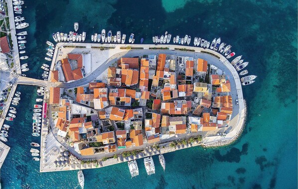 Luchtbeeld van een kustplaatsje met een jachthaven, compacte woningen en een bochtige weg.