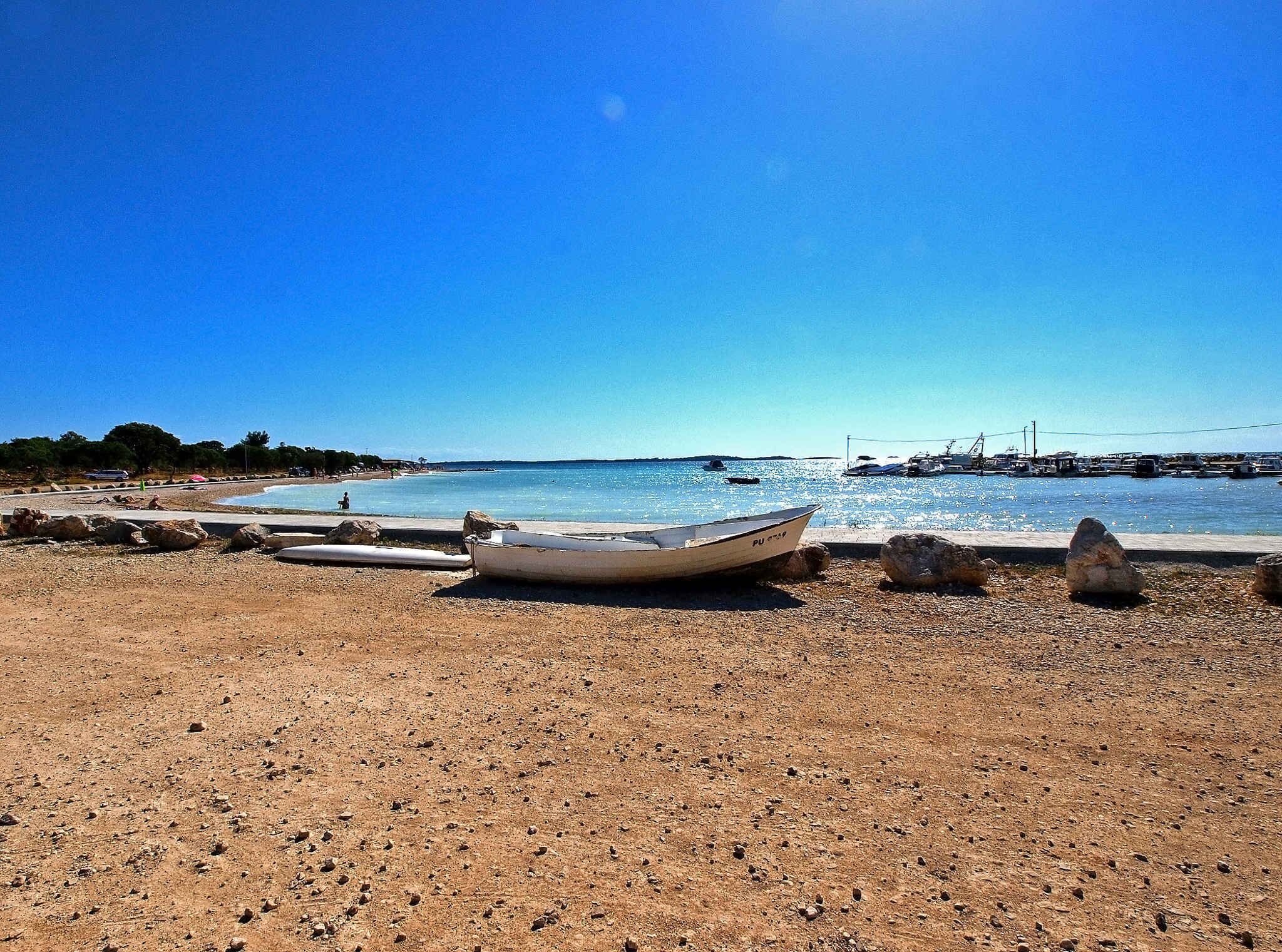 A beach with a boat, pebbles, and a clear blue sky.
