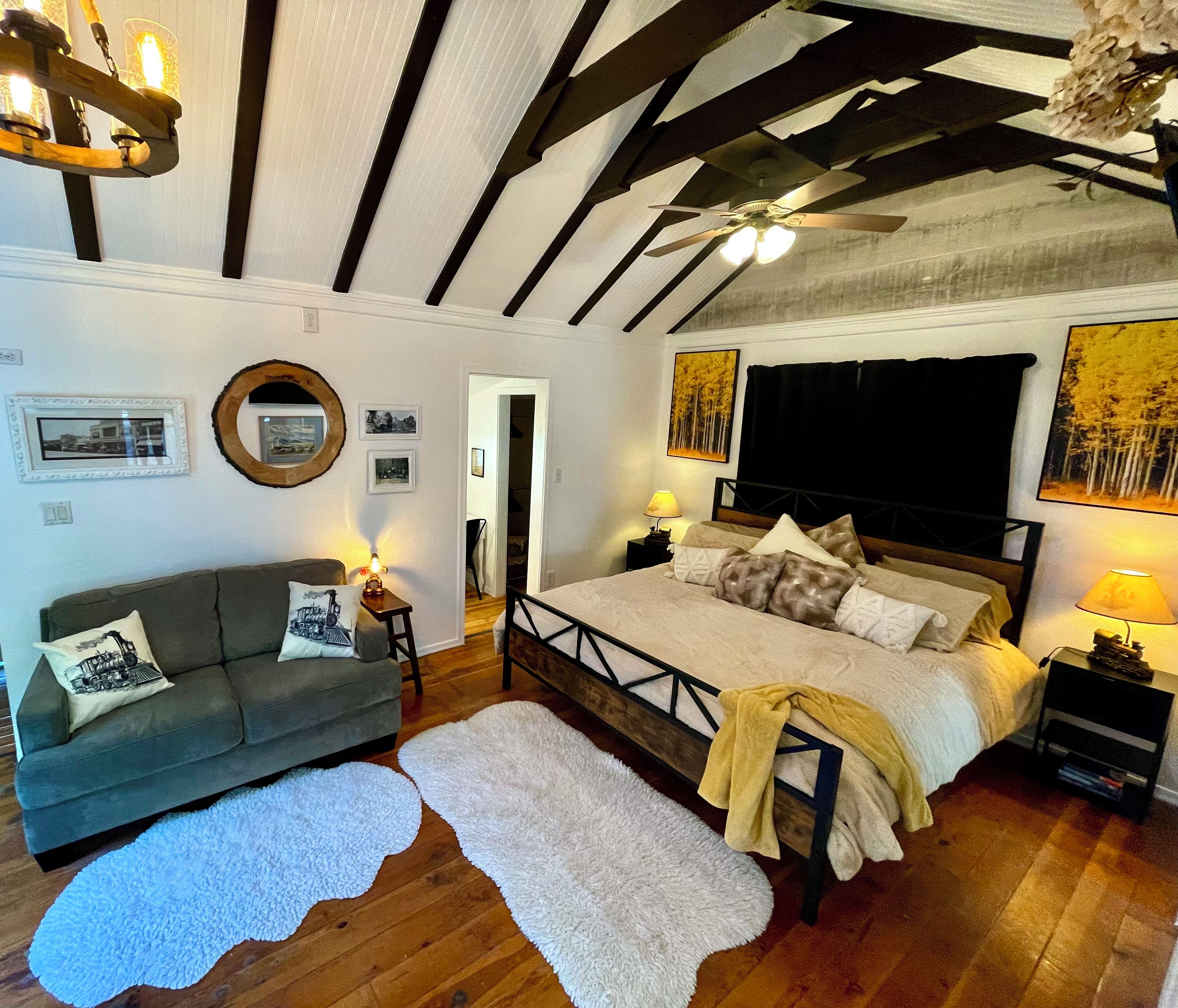 Ein Schlafzimmer mit einem Bett, einem Sofa, einem Spiegel und einem Deckenventilator.