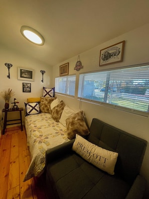 Um quarto acolhedor com cama, sofá e janela com persianas. Há quadros nas paredes e uma chave decorativa na parede.