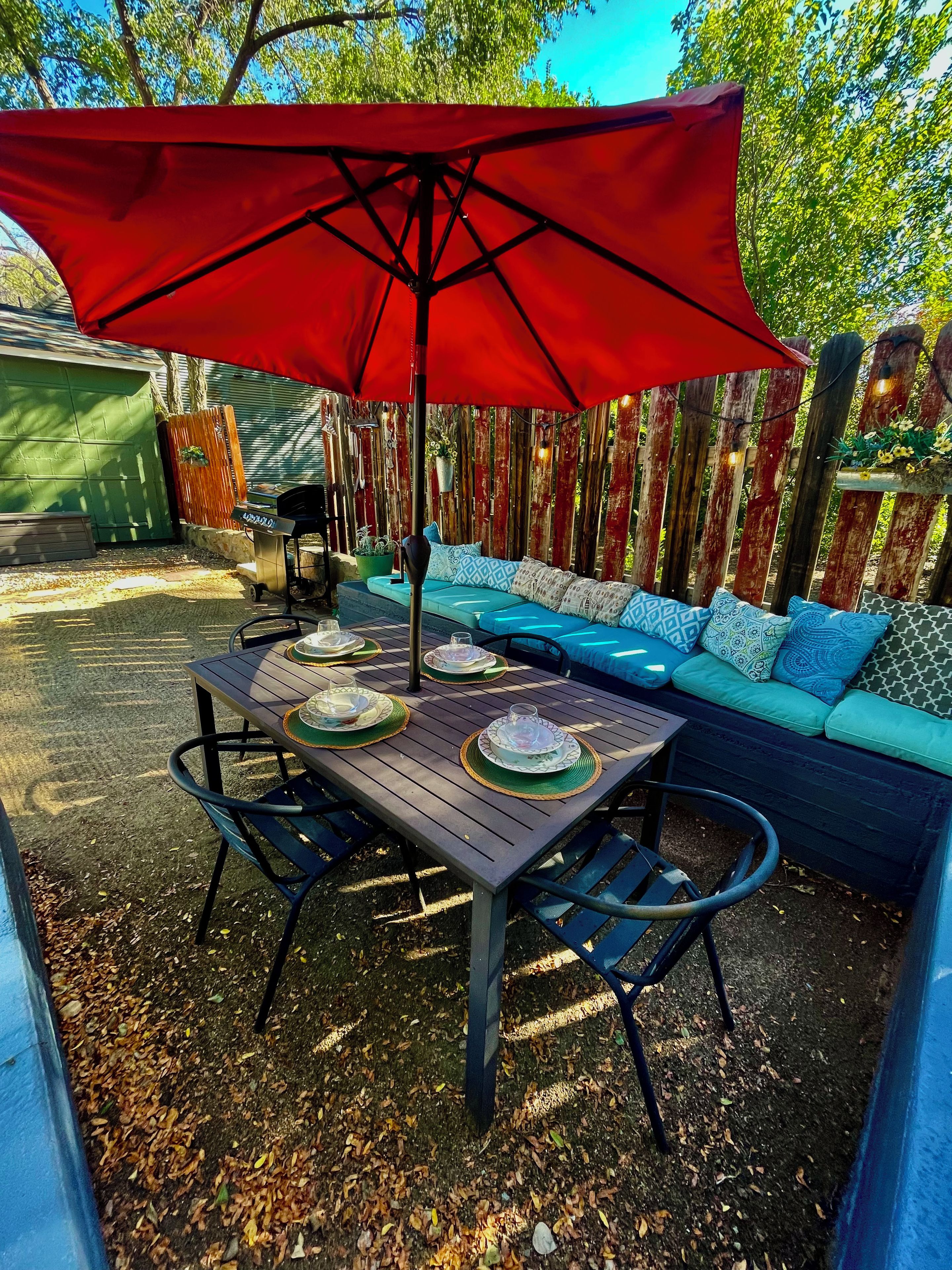 Une terrasse extérieure avec une table dressée pour le repas, un canapé et un parasol rouge.