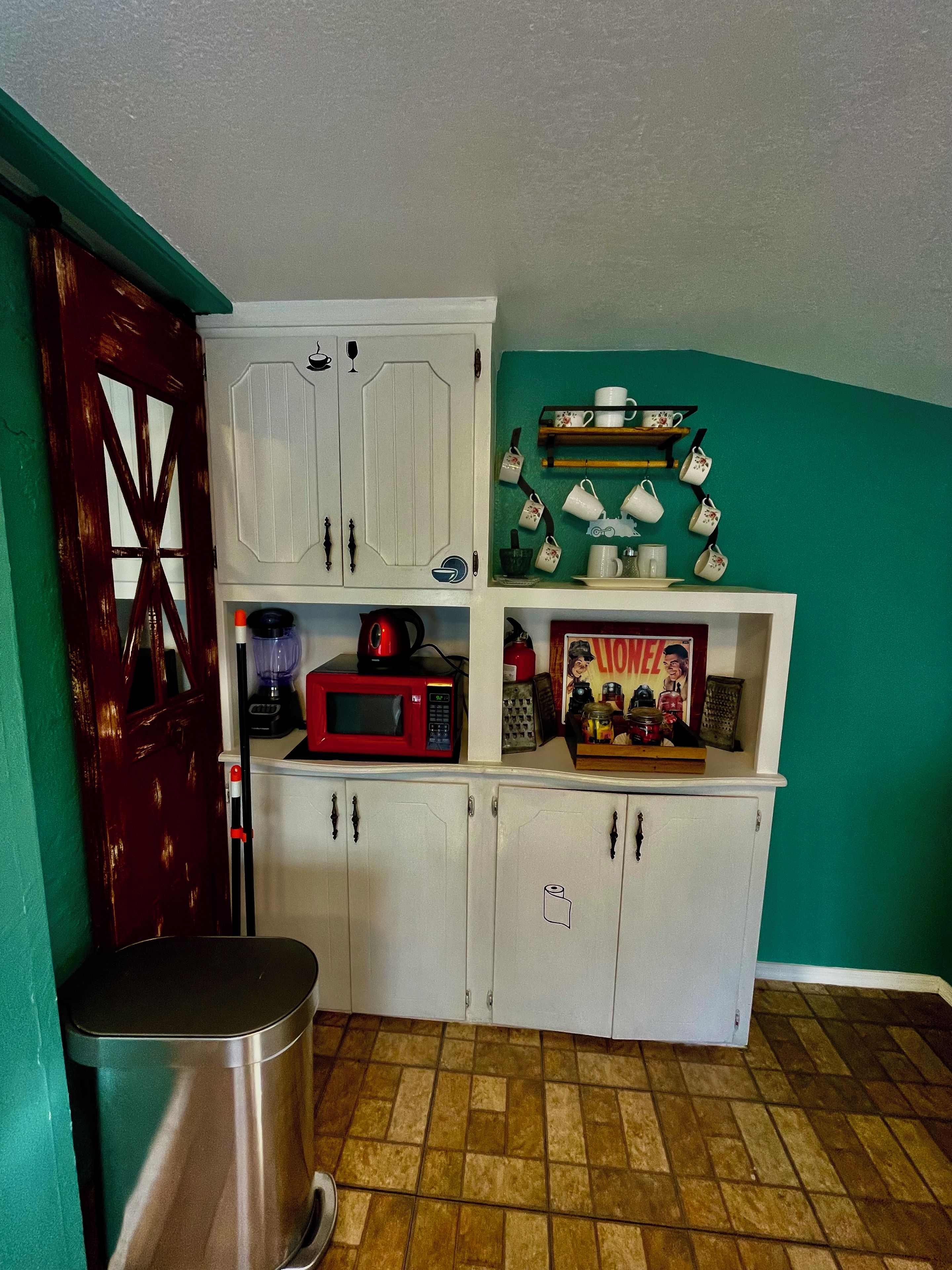 A compact kitchen with white cabinets, a red microwave, and a green wall.