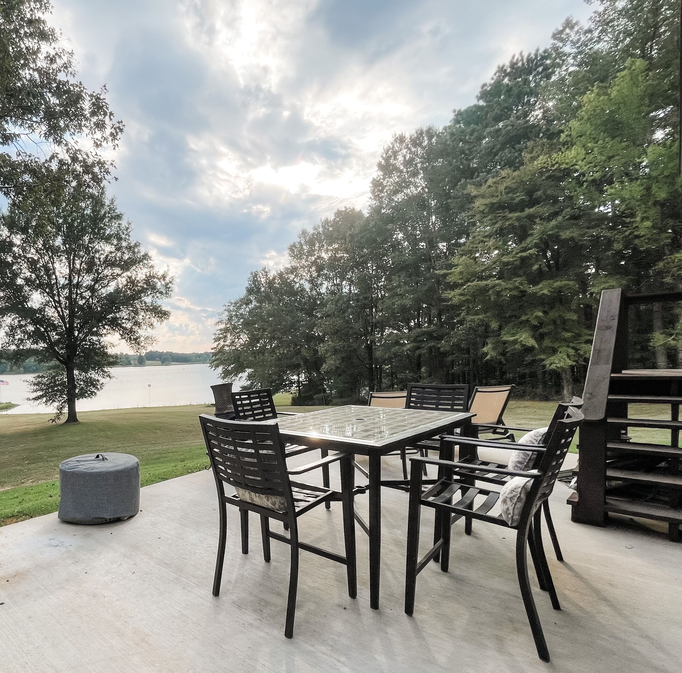 An outdoor patio with a table and chairs, overlooking a lake and surrounded by trees.