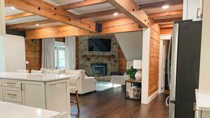 A modern kitchen with white cabinetry, a stone fireplace, and a wooden ceiling. - Waverly Lakehouse - private cabin, lake view, close to 
Old Waverly/Mossy Oak (West Point)