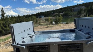 Un jacuzzi con revestimiento de piedra, rodeado por un paisaje natural con un lago y bosque.