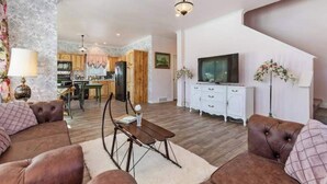 Una sala de estar con un sofá, una mesa de centro y un televisor. Se ve una cocina al fondo.