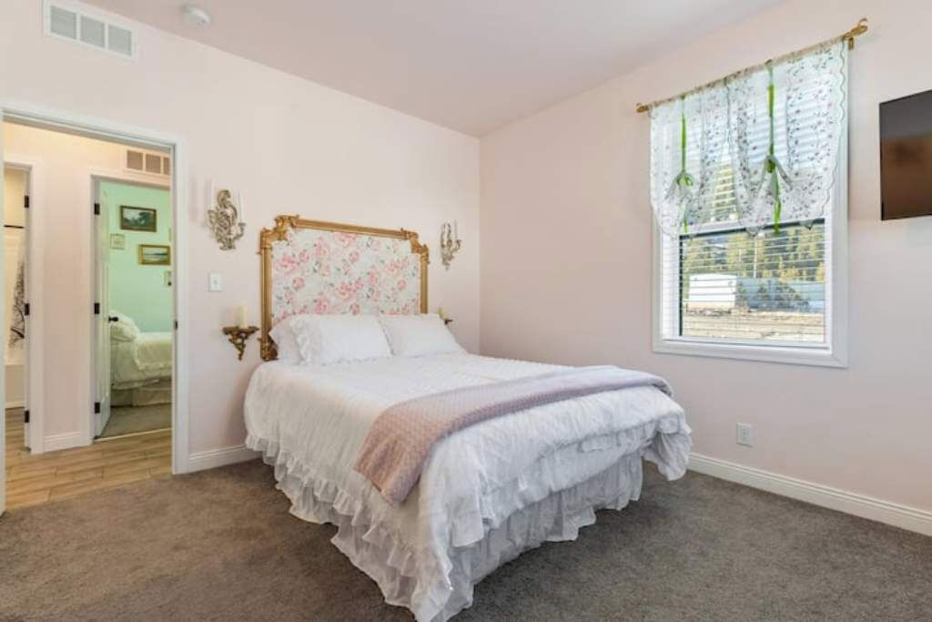A bedroom with a large bed, a window with floral curtains, and a door leading to another room.