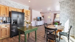Una cocina moderna con armarios de madera, un refrigerador negro y un comedor con una mesa verde y sillas negras.