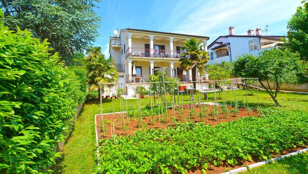 A two-story building with a balcony and a garden in front. - Holiday apartment with air conditioning and barbecue facilities (Poreč)