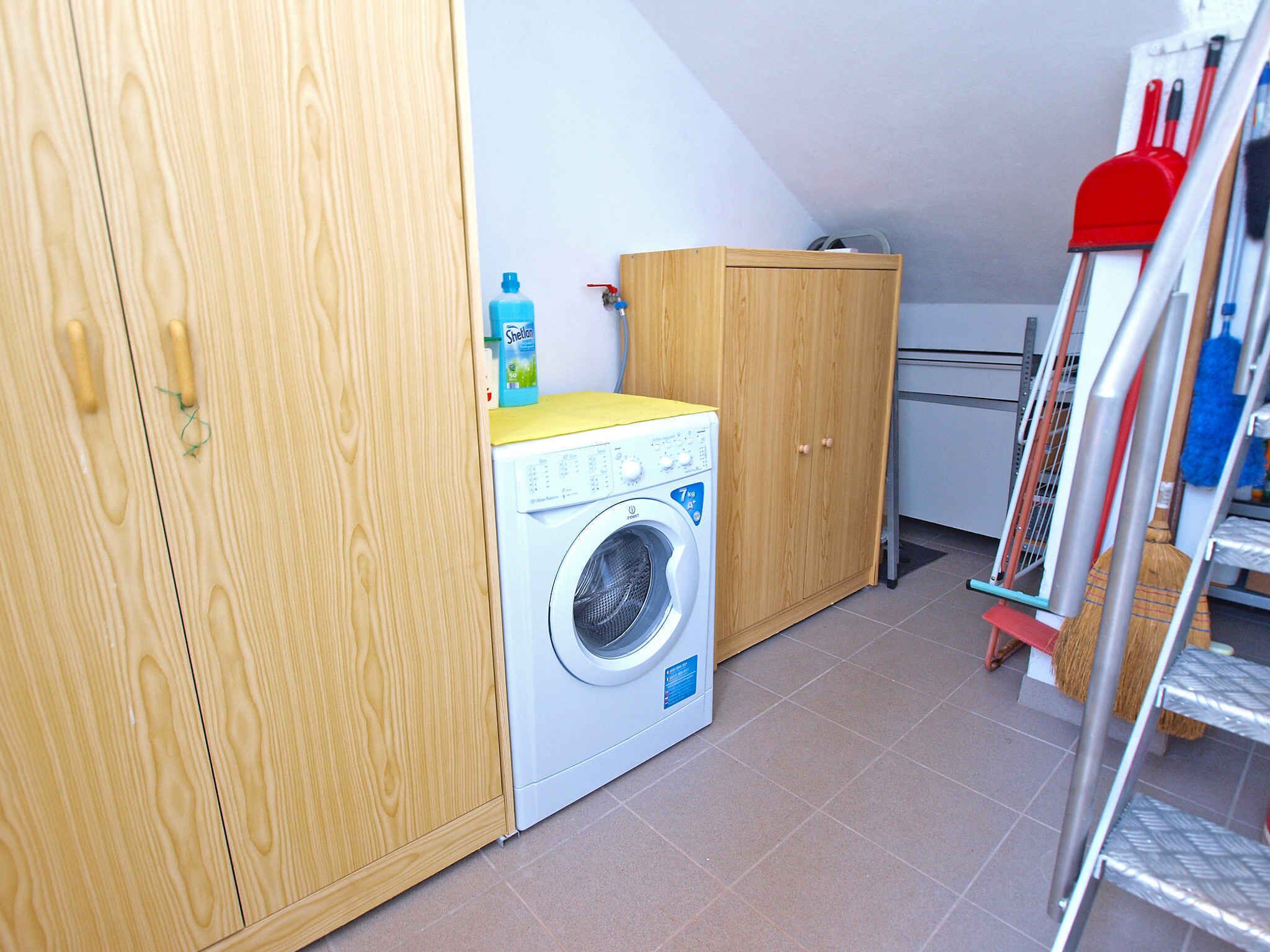A laundry room with a washing machine, wooden cabinets, and a broom.
