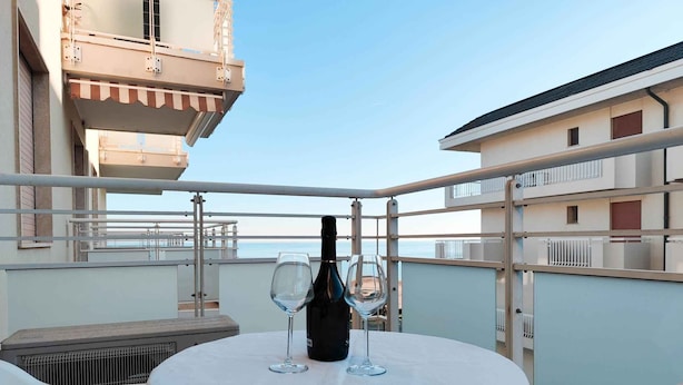A balcony with a table set for two, a bottle of wine, and two wine glasses. - Holiday apartment (Lido di Jesolo)