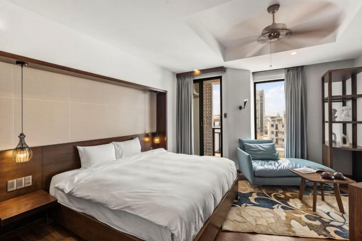 A hotel room with a bed, a sofa, a small table, and a balcony with a view.