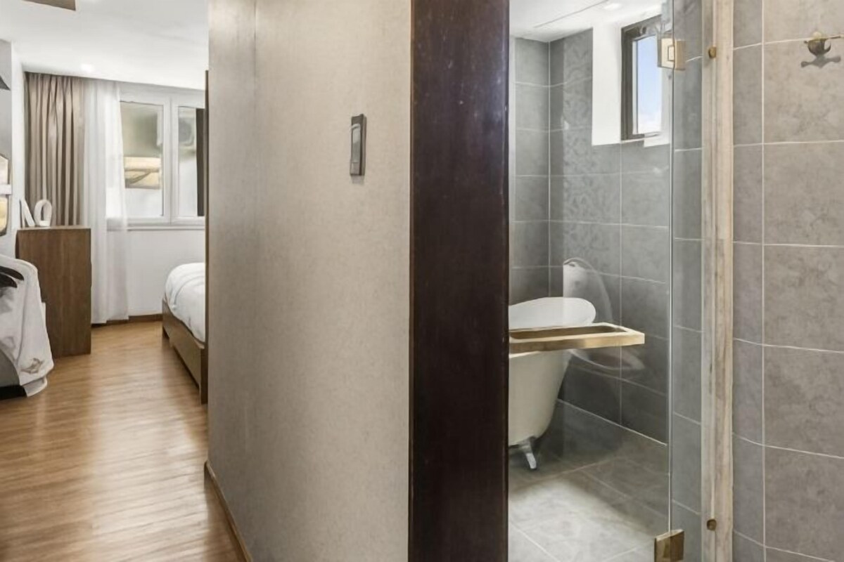 Una habitación de hotel con cama, mesita de noche, zona de ducha y ventana.
