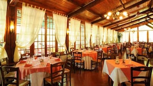 Un restaurante con techos de madera y amplios ventanales con cortinas blancas. Las mesas están preparadas con manteles blancos y servilletas rojas.