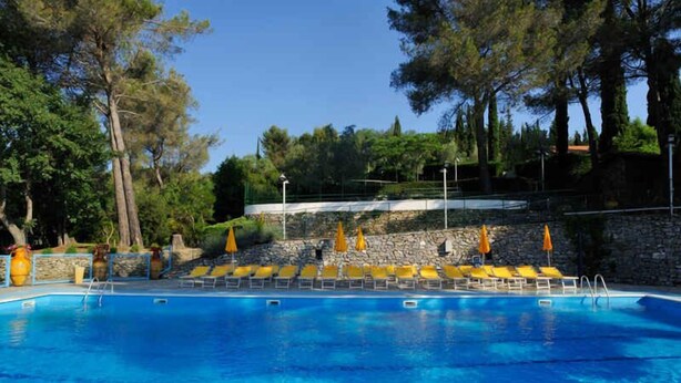 Una piscina con agua cristalina azul, rodeada de muros de piedra y sillas de descanso amarillas.