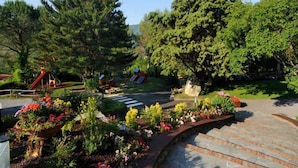 Un parque con un área de juegos, un árbol grande y un parterre floral.
