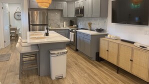 Een moderne keuken met grijze kastjes, een roestvrijstalen koelkast, een inbouwoven, een magnetron en een grote flatscreen-tv aan de muur.