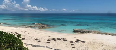Een strand met helder turquoise water, een zandstrand en verspreide rotsen.